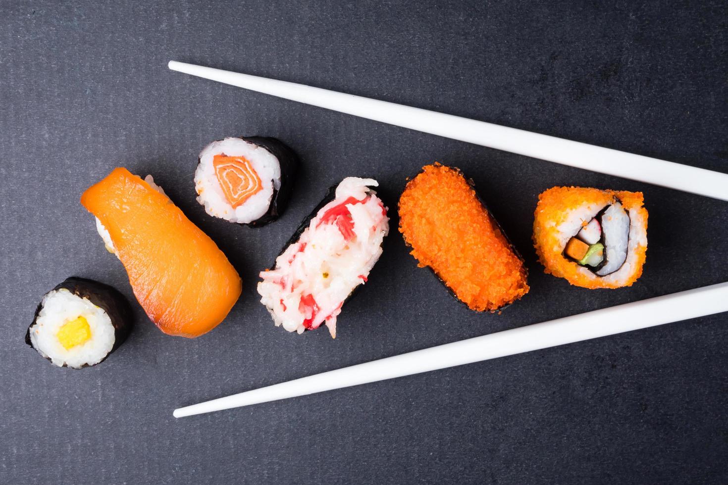 topp se av sushi uppsättning och ätpinnar på svart bakgrund, japansk mat. foto