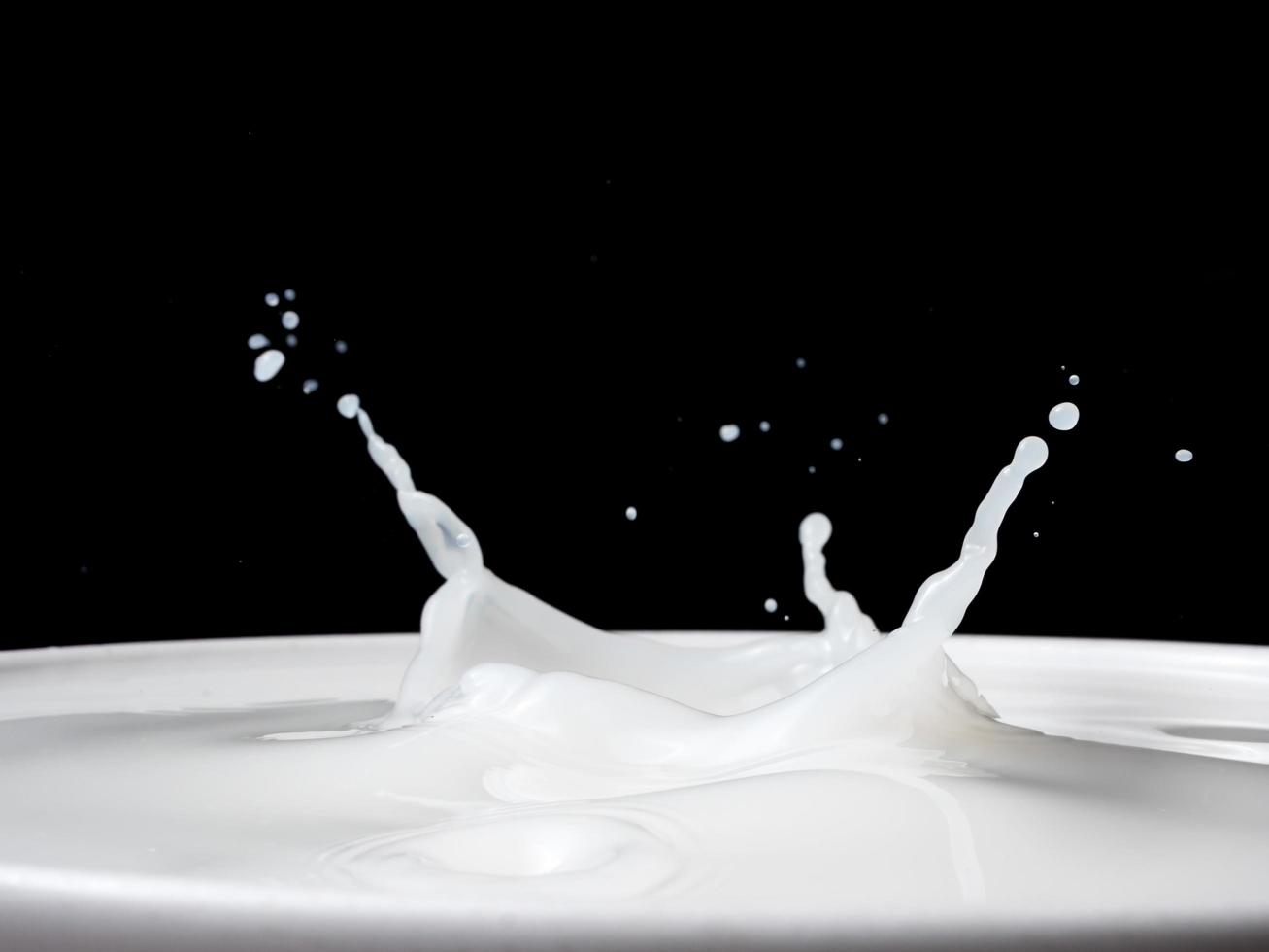 stänk av mjölk från en kopp på svart bakgrund. foto