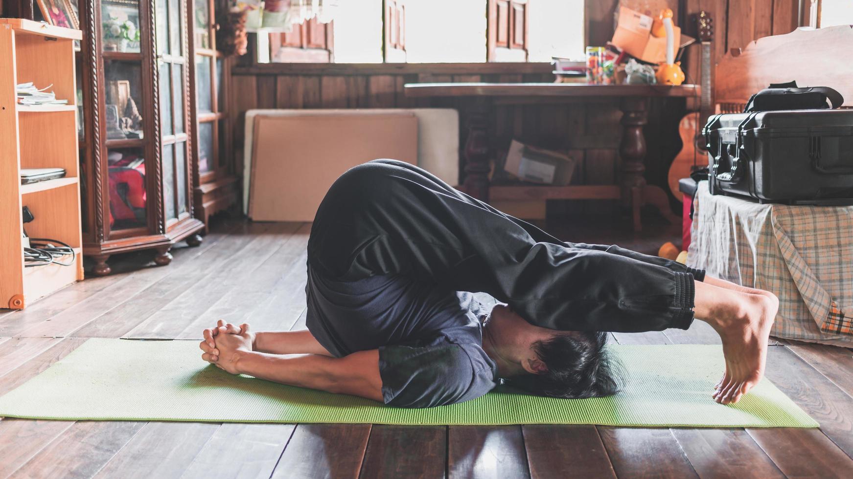 ung asiatisk man praktiserande yoga i en trä- rum Sammanträde i utgör plog utgör på en grön yoga matta på en trä- hus. friska liv begrepp foto