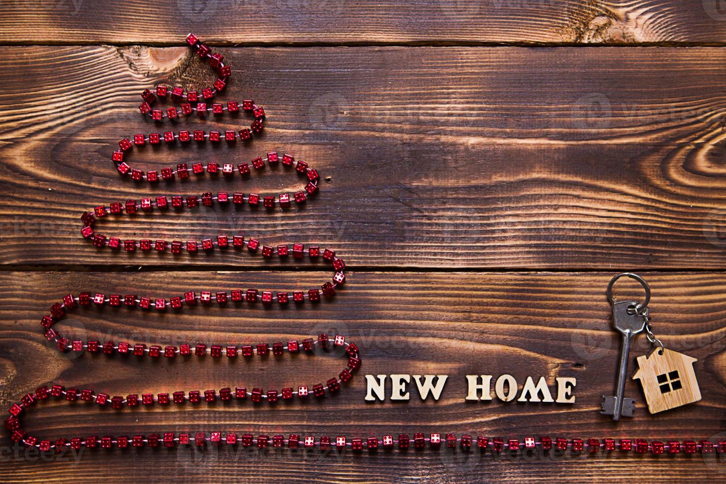 julgran på träbakgrund med nyckel till huset och nyckelring med inskription på engelska nya hem. bygga eller köpa hus på nyår. inteckning, fastighetsuthyrning. kopiera utrymme, platt foto