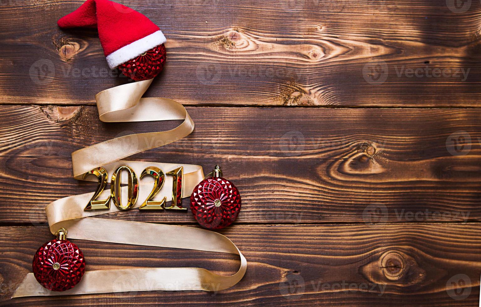 en julgran gjord av guldband med siffrorna 2021 är dekorerad med röda ballonger på en mörk träbakgrund. platt låg. utrymme för text. nytt år, tomteluva. foto