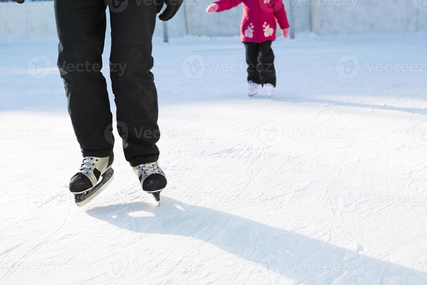 pappa lär sin lilla dotter att åka skridskor på en skridskobana på innergården till flera våningar i staden. frostig vinter solig dag, aktiv vintersport och livsstil foto
