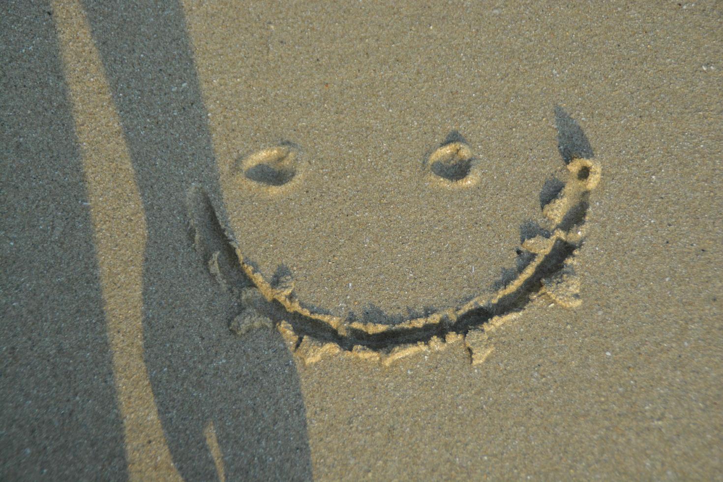 en smiley ansikte teckning på en sand. med någon skugga. foto