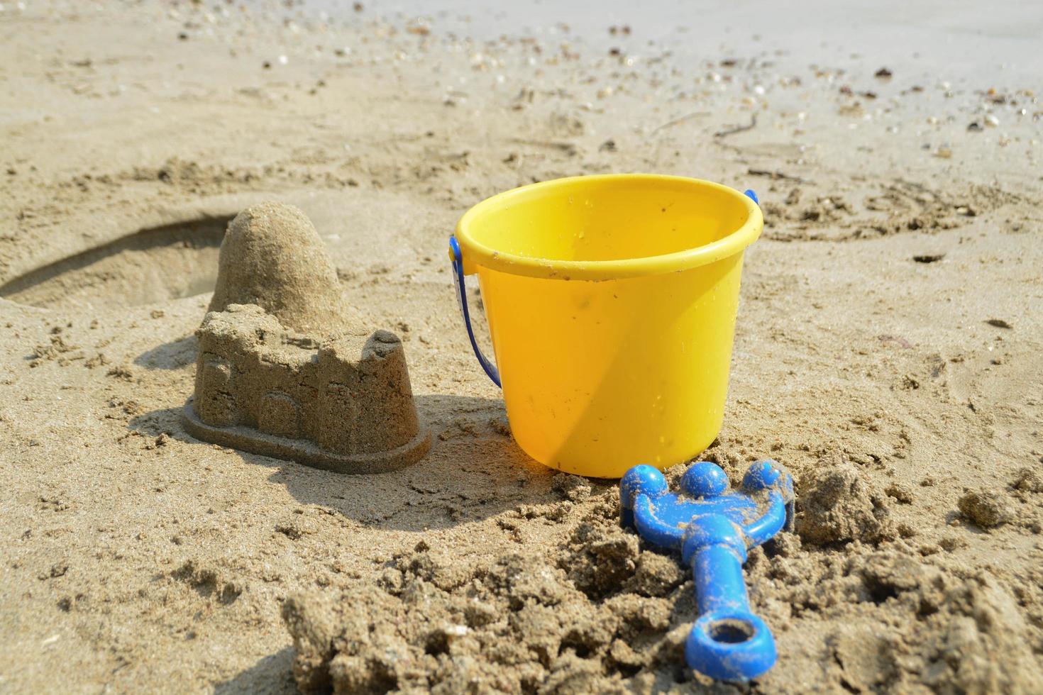 sand slott på de strand med gul plast korg barn leksaker och blå räfsa barn leksak. foto