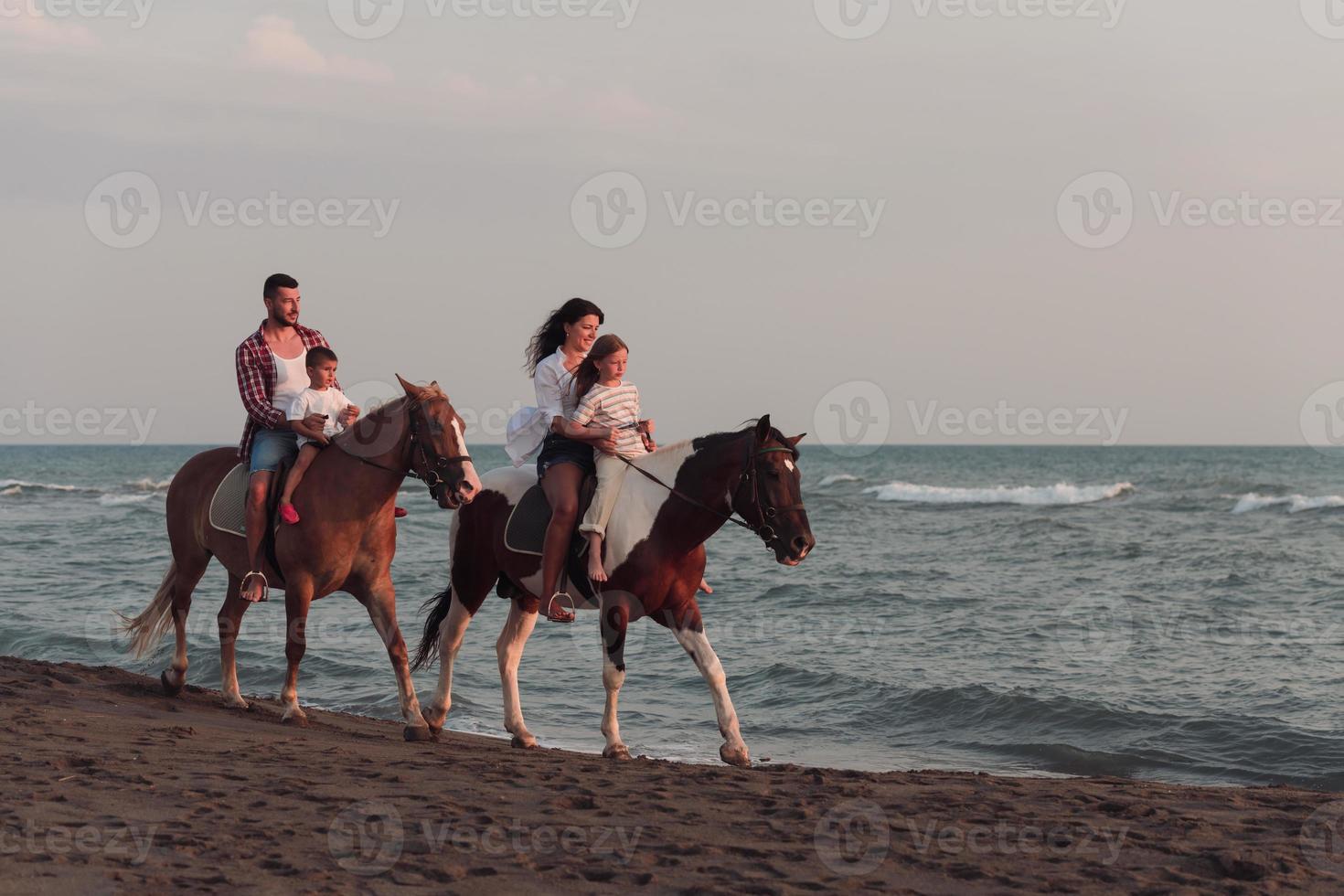 de familj spenderar tid med deras barn medan ridning hästar tillsammans på en skön sandig strand på solnedgång. foto