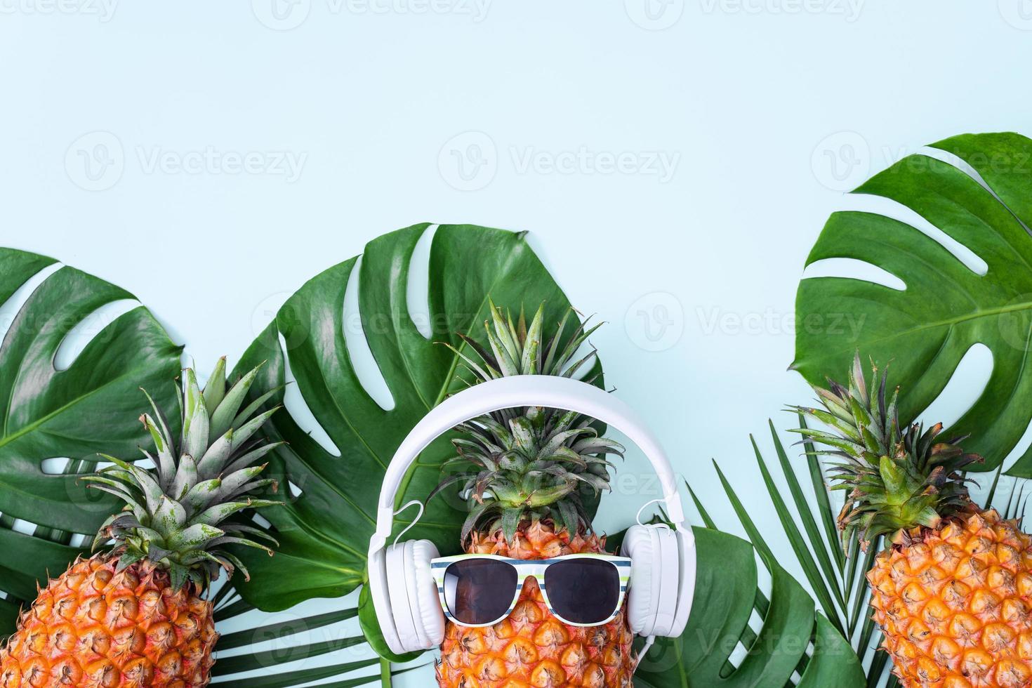 rolig ananas som bär vita hörlurar, koncept för att lyssna på musik, isolerad på färgad bakgrund med tropiska palmblad, ovanifrån, platt lekmannadesign. foto