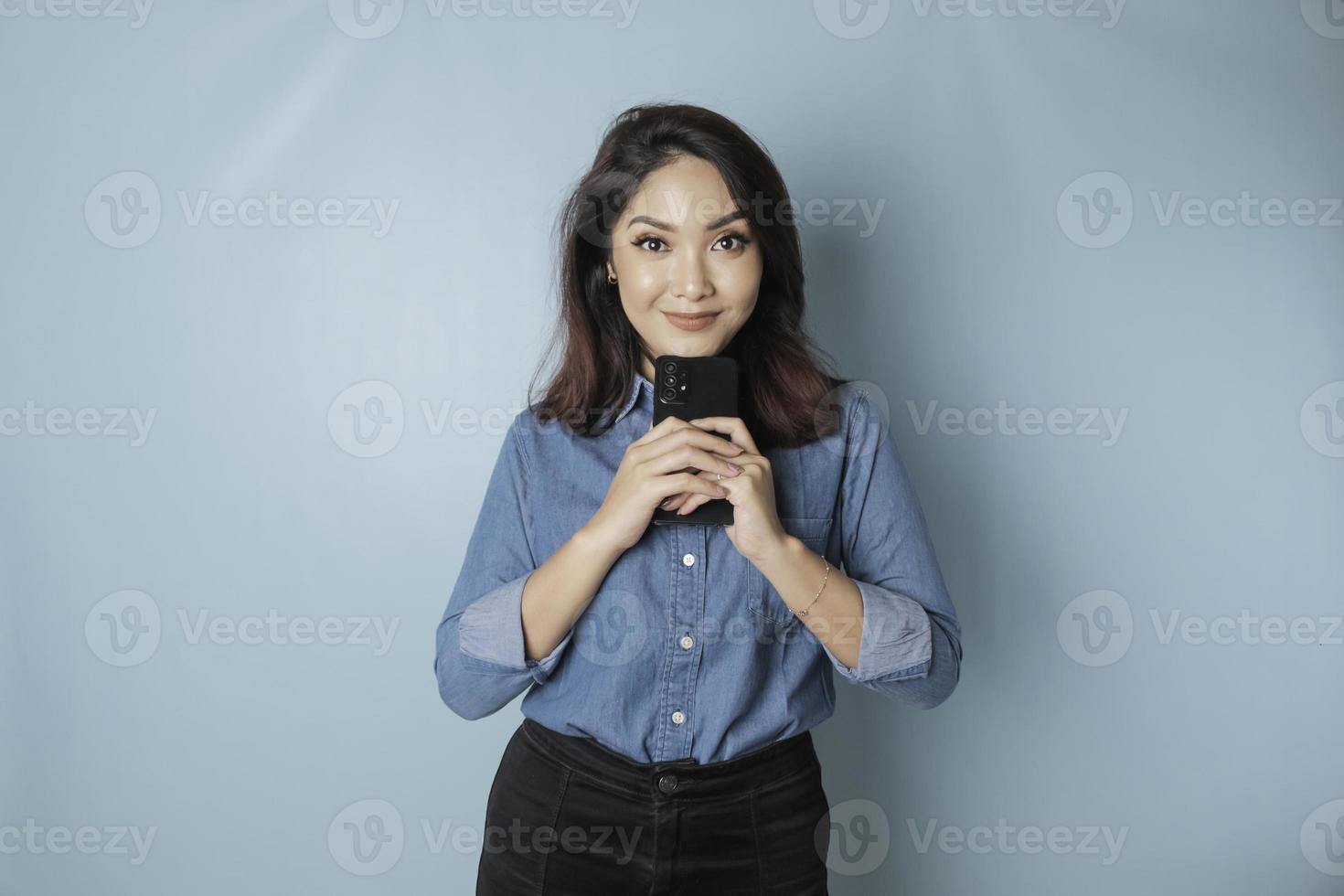 porträtt av en omtänksam ung tillfällig flicka bär en blå skjorta ser åt sidan medan innehav smartphone isolerat över blå bakgrund foto