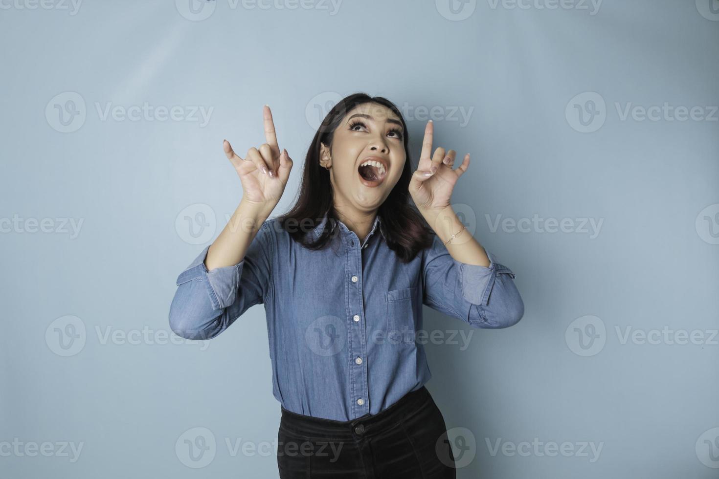 chockade asiatisk kvinna bär blå skjorta pekande på de kopia Plats uppåt, isolerat förbi blå bakgrund foto