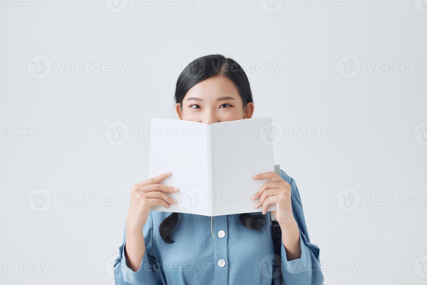 Lycklig fundersam flicka innehav vit anteckningsbok, beläggning halv av ansikte, ser uppmärksamt på kamera, foto