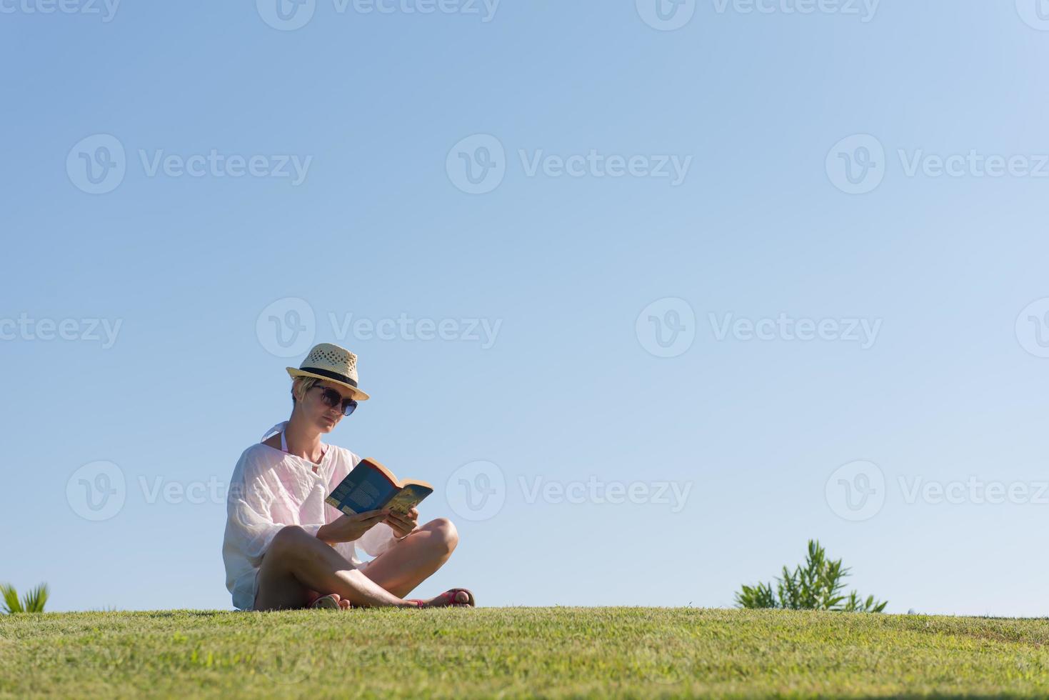 kvinna liggande och läsning henne favorit bok på en äng täckt med färsk grön gräs på en solig sommar eller vår dag. foto