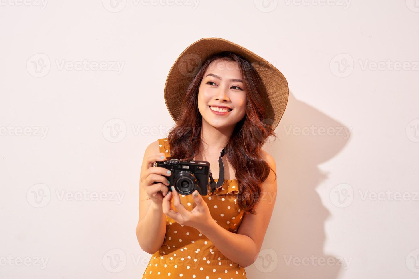 porträtt av glad leende ung kvinna tar Foto med inspiration och bär sommar klänning. flicka innehav retro kamera. modell Framställ på beige bakgrund i hatt