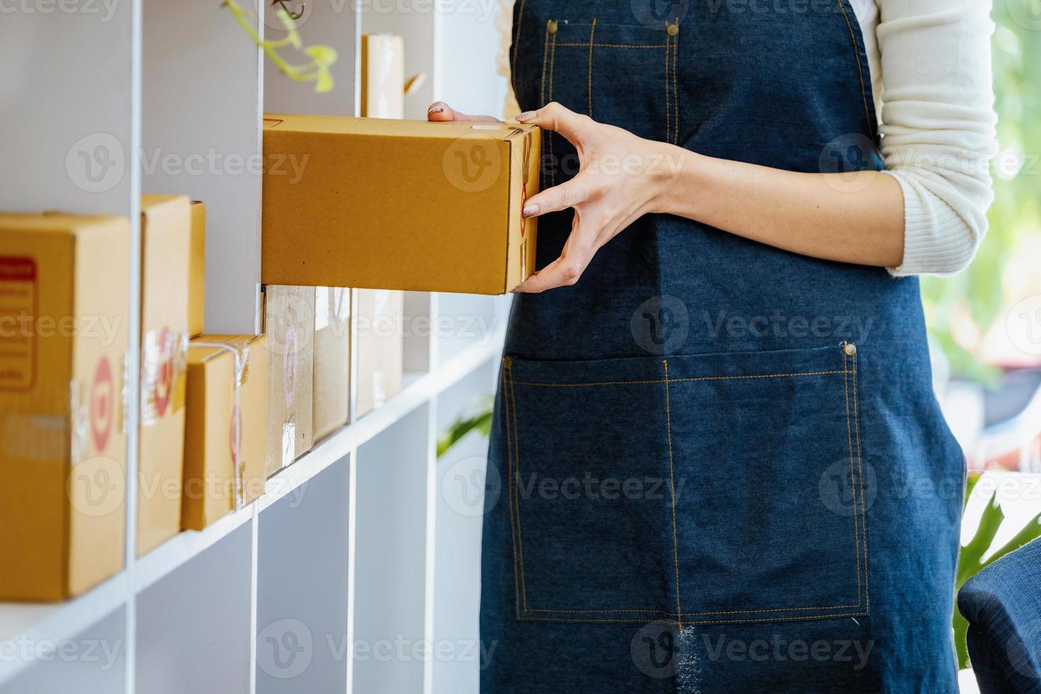 arbete från Hem. Lycklig kvinnor försäljning Produkter uppkopplad börja små företag ägare är plockning upp paket lådor till packa kund order och förbereda dem för porto. foto