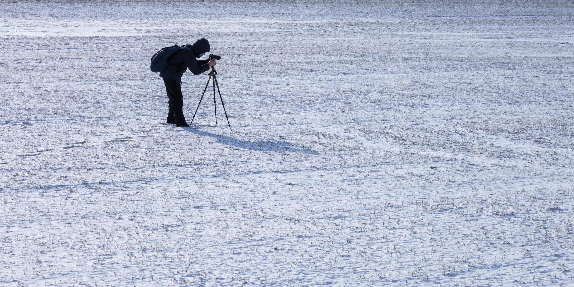 fotograf med en stativ i snöig fält tar bilder av landskap, fotspår i snö foto