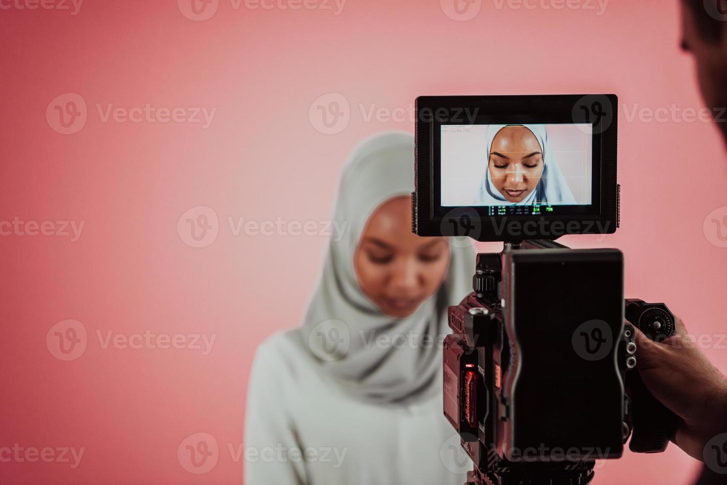 videographer i digital studio inspelning video på professionell kamera förbi skytte kvinna muslim kvinna bär hijab scarf plast rosa bakgrund. foto
