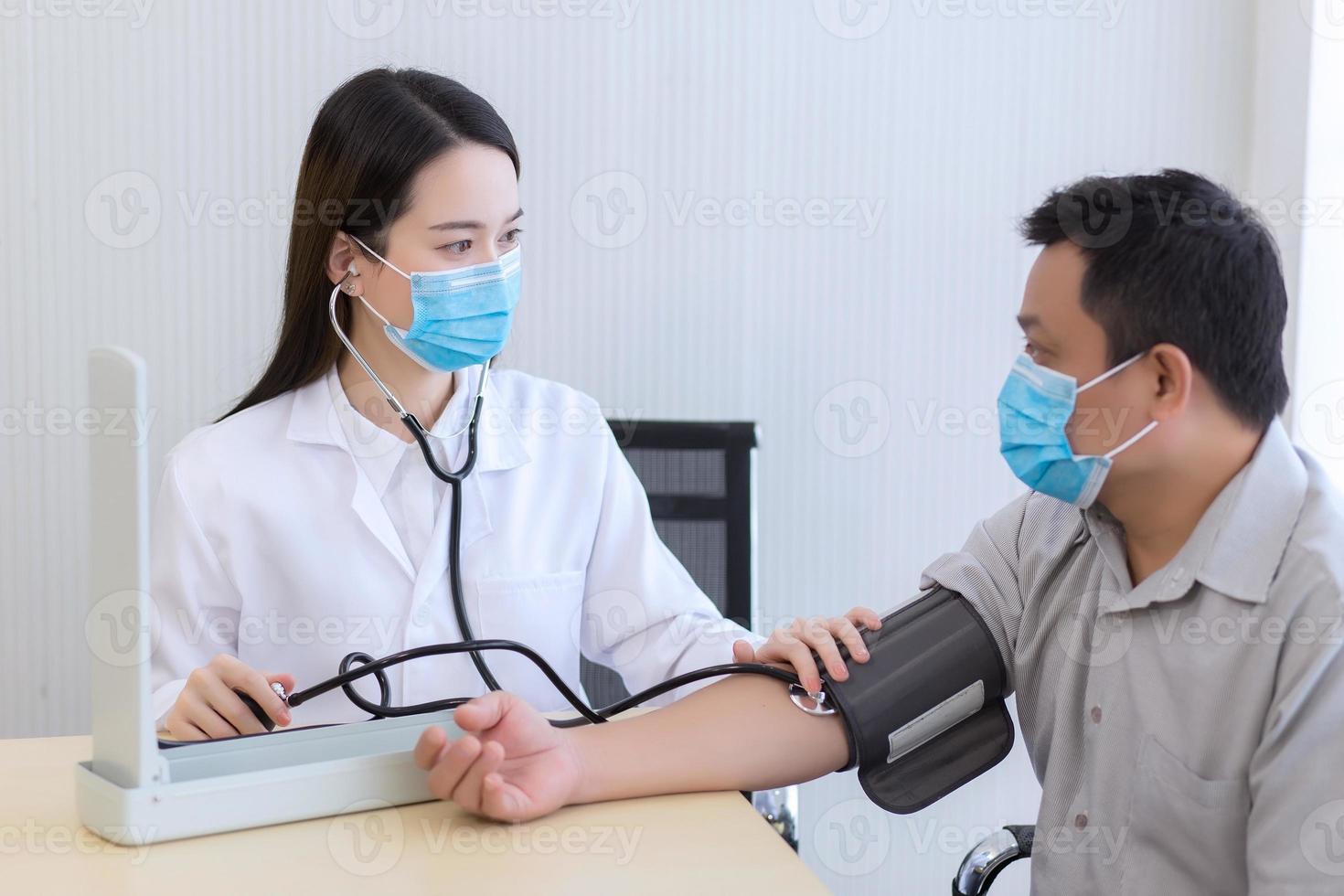 asiatisk kvinna läkare användningar stetoskop och en blod tryck bilkörning till mäta blod tryck av de man patient. i sjukvård begrepp, både ha på sig medicinsk ansikte mask till skydda patogener eller korona virus foto