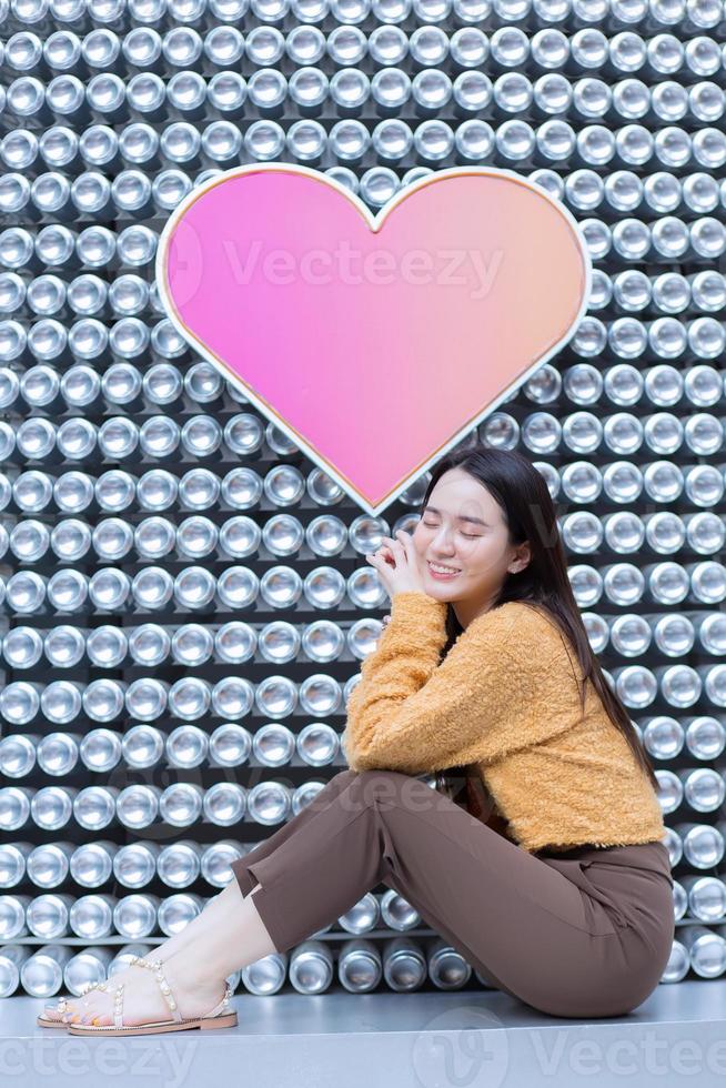 asiatisk vacker kvinna med långt hår sitter och stänger ögonen i hjärtat bakgrund som alla hjärtans dag koncept. abstrakt bakgrund foto