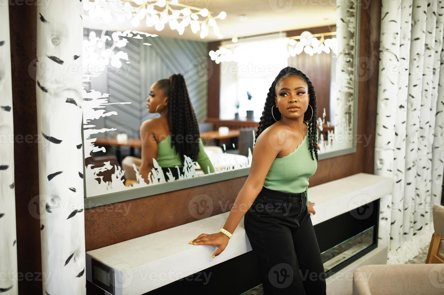 porträtt av attraktiv ung afrikansk amerikan kvinna bär i grön Tröja och svart jeans utgör mot spegel. foto