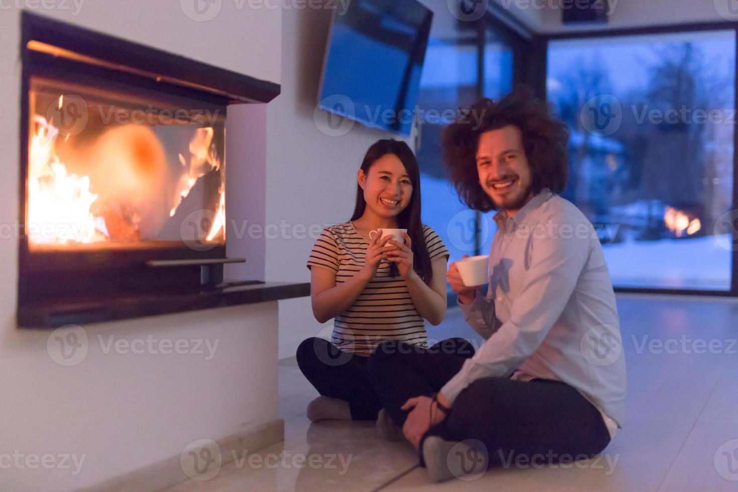 lyckligt multietniskt par som sitter framför den öppna spisen foto