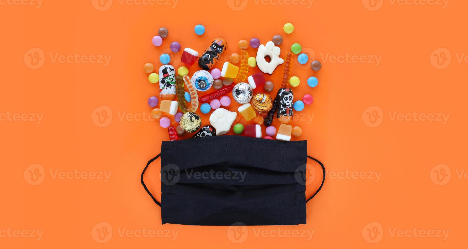 svart medicinsk mask tycka om handla gåva väska full av spillts blandad godis, traditionell halloween choklad och gelé maskar. orange baner bakgrund med kopia Plats. foto