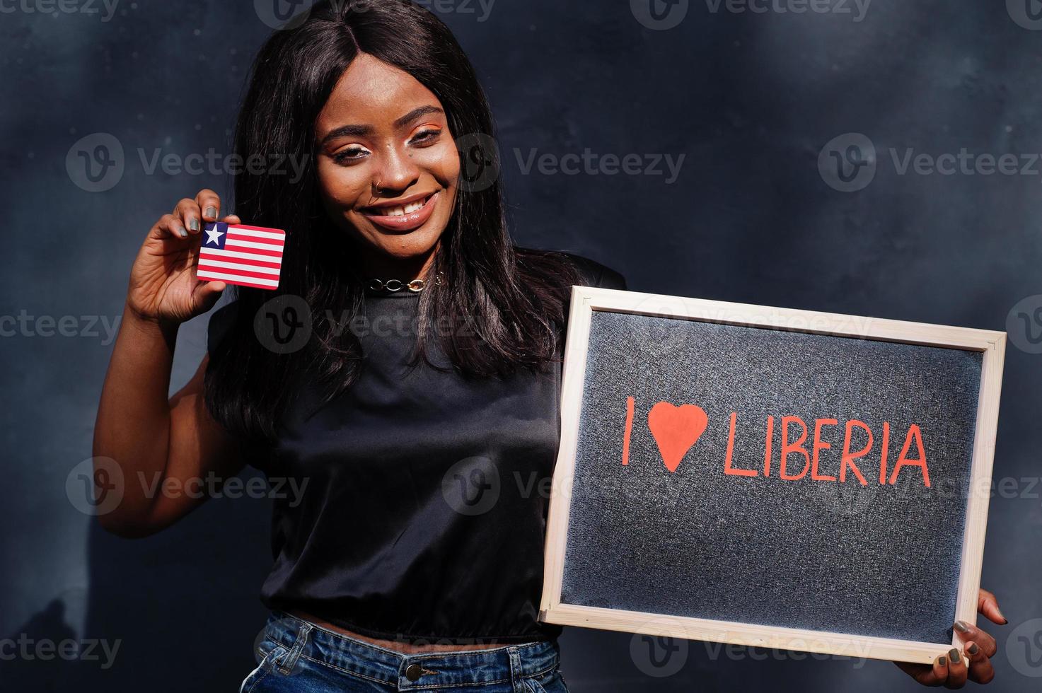 jag kärlek liberia. modern afrikansk kvinna håll svarta tavlan med liberian flagga. foto