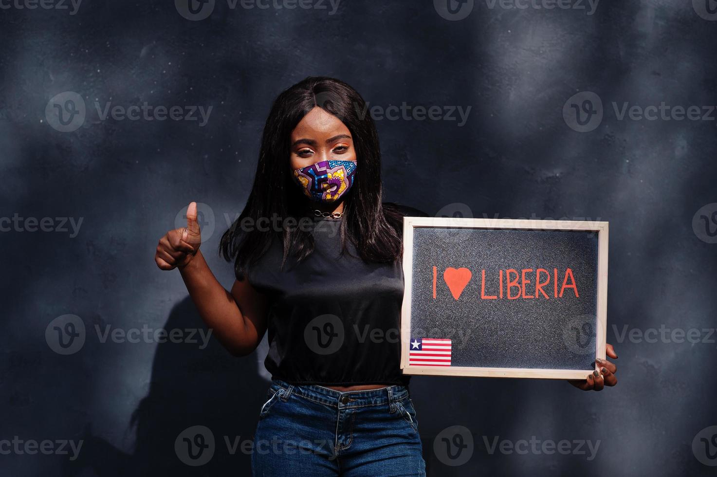 jag kärlek liberia. modern afrikansk kvinna, ha på sig hand tillverkad ansikte mask håll svarta tavlan med liberian flagga. foto