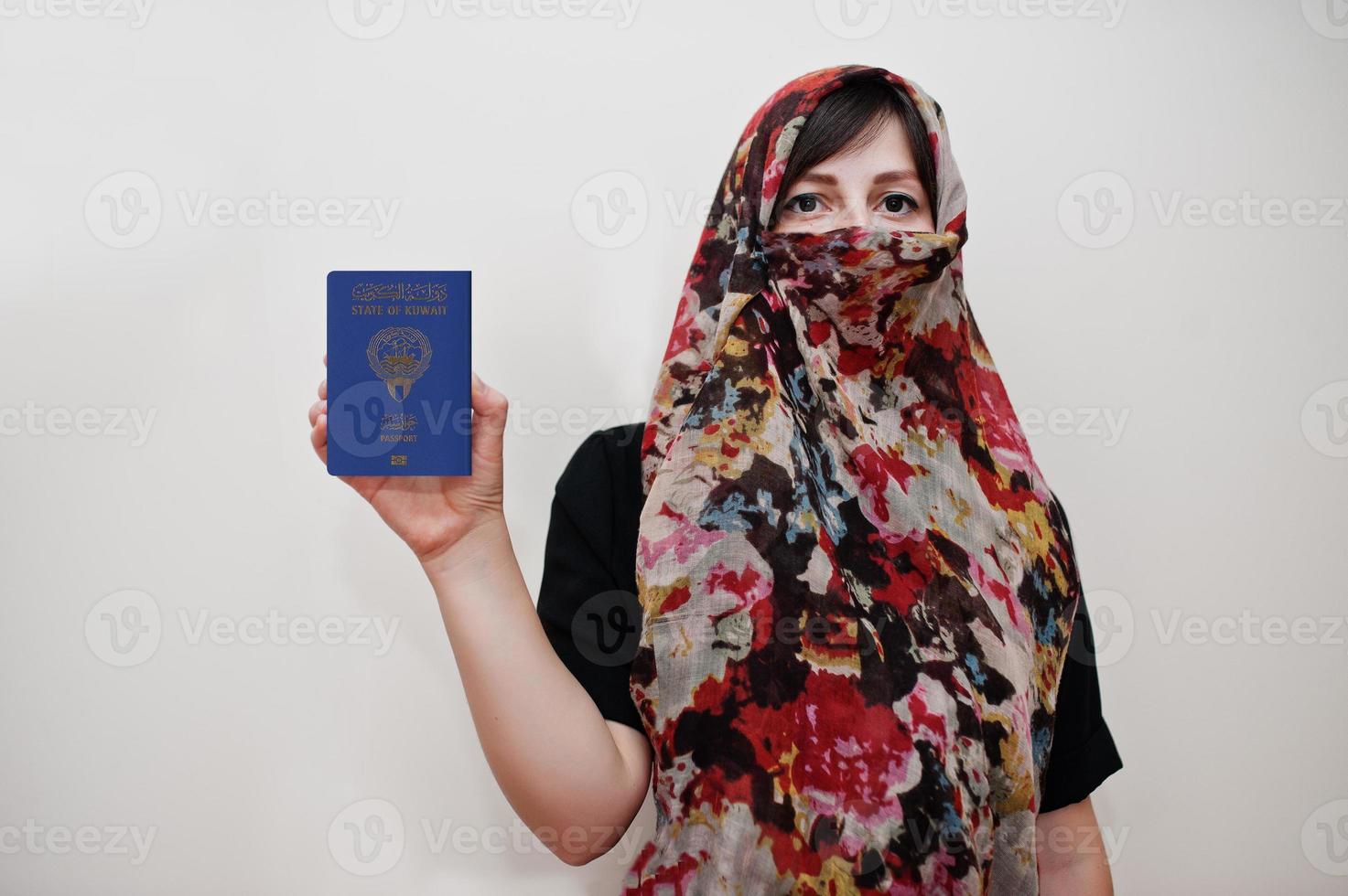 ung arab muslim kvinna i hijab kläder håll stat av kuwait pass på vit vägg bakgrund, studio porträtt. foto