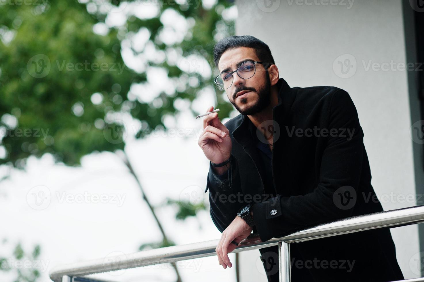 mitten östra entreprenör ha på sig svart täcka och blå skjorta, glasögon mot kontor byggnad rökning cigarett. foto