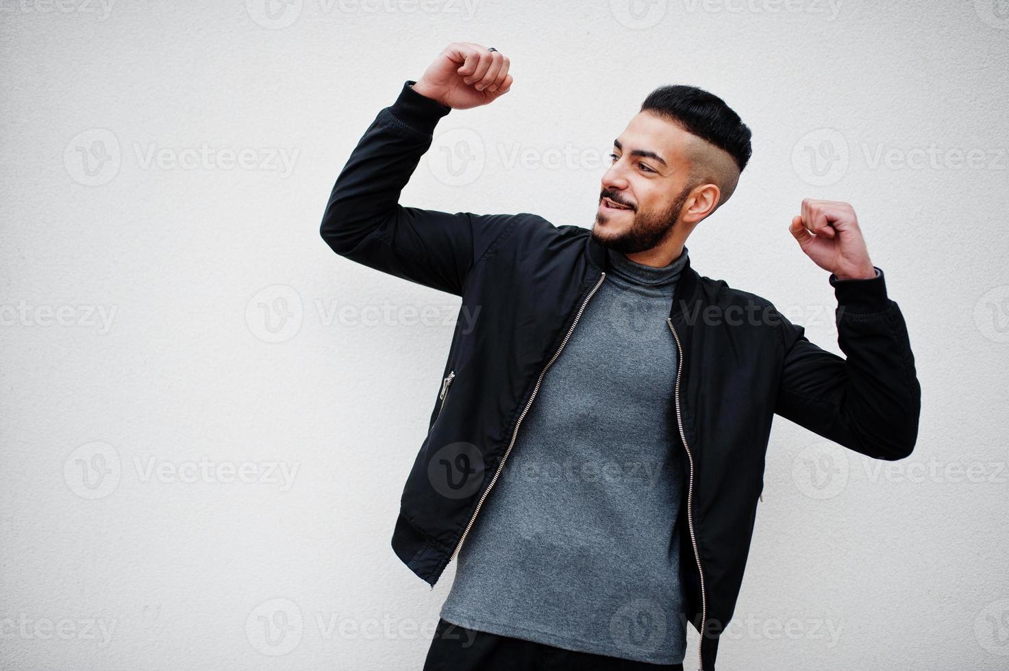 porträtt av eleganta nöjd arab skägg man ha på sig grå turtleneck och svart jacka. arab modell kille. foto