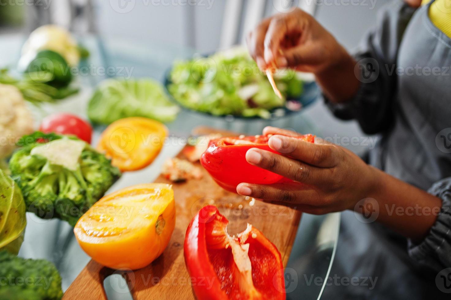 afrikansk amerikan kvinna framställning friska mat på Hem kök. hon nedskärningar röd peppar. foto