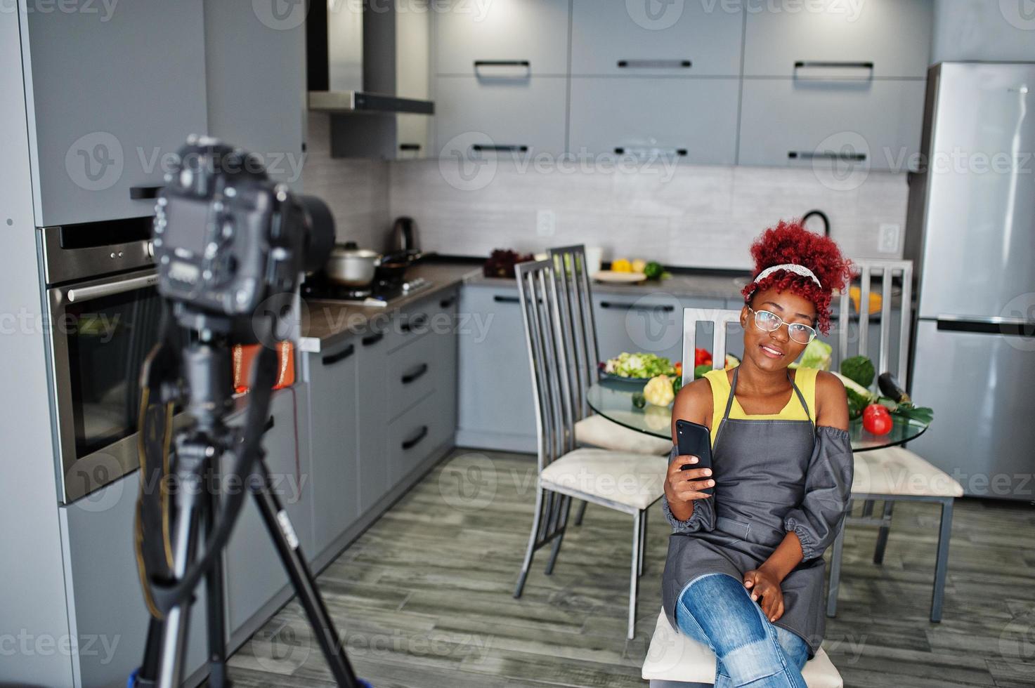 afrikansk amerikan kvinna filmning henne blog utsända handla om friska mat på Hem kök och ser på telefon. foto