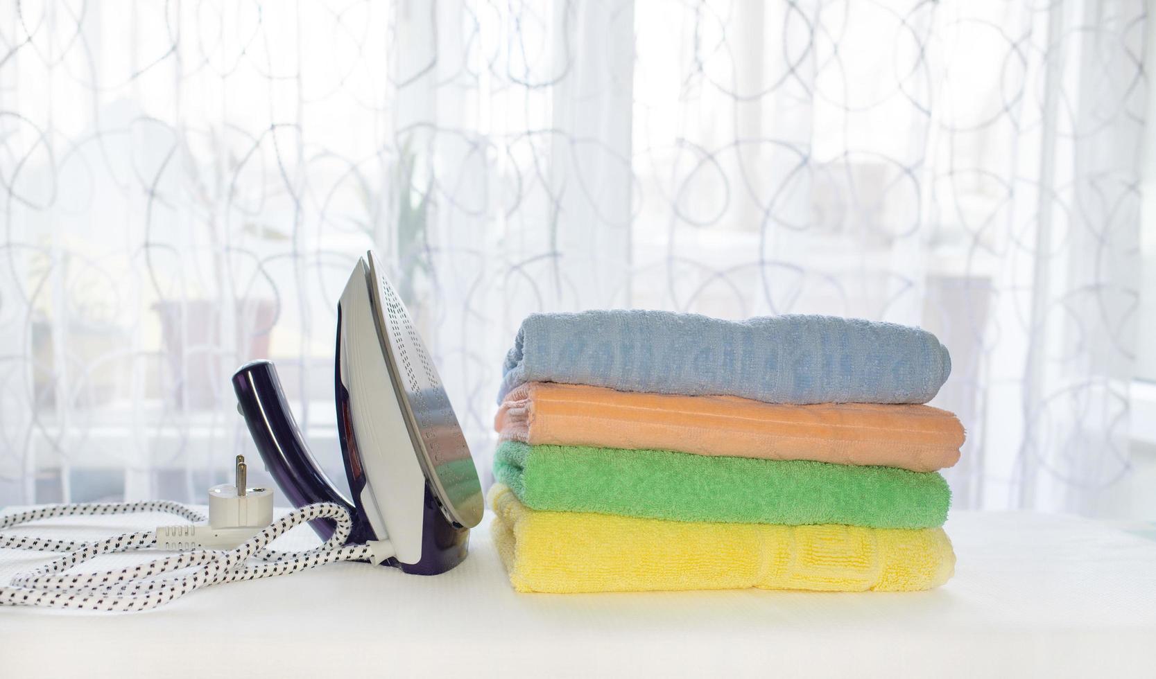handdukar vikta i en rulla och ett järn efter strykning på ett strykning styrelse. hushållning begrepp foto