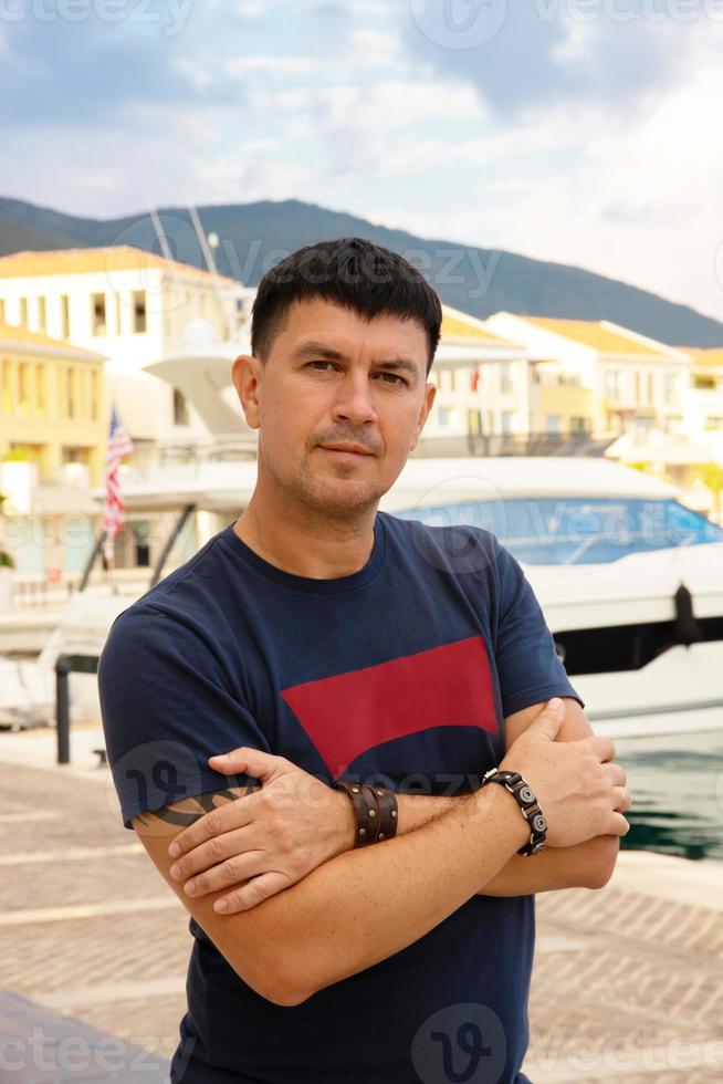 caucasian man i en blå t-shirt poser nära en Yacht i de hamn, tivat, montenegro. foto