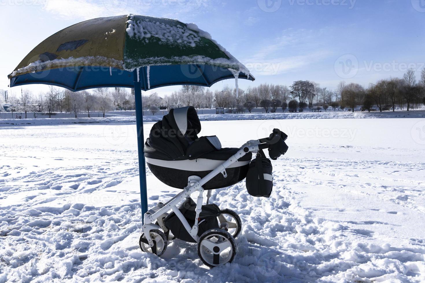 bebis transport förbi de sjö i vinter. strand under de snö och ett paraply från de Sol. de begrepp av vinter- högtider med barn. foto