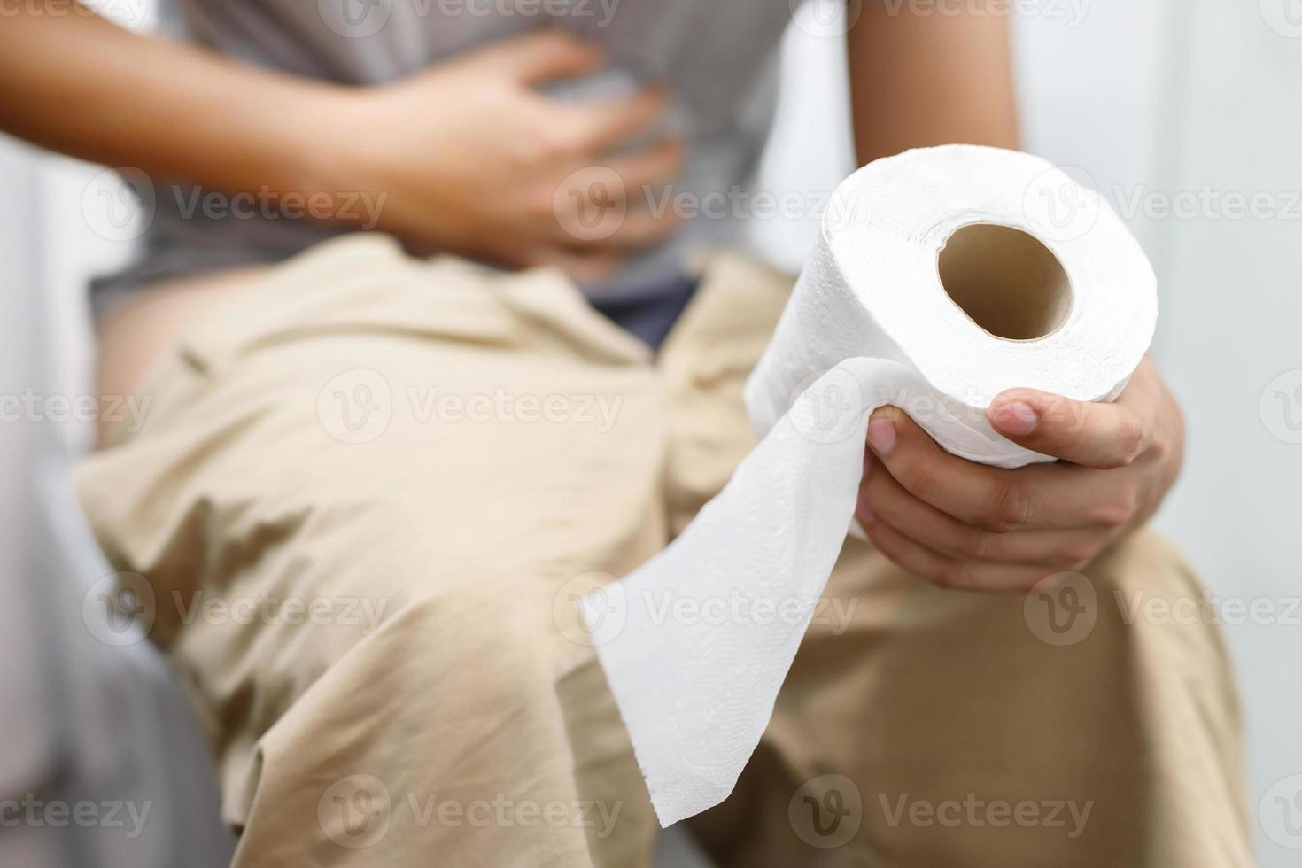 man lider från diarre hand håll vävnad papper rulla i främre av toalett skål. förstoppning i badrum. behandling mage smärta och hygien, hälsa vård foto
