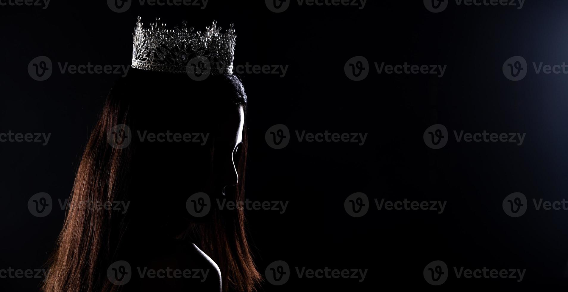 porträtt av Fröken festtåg skönhet tävling i paljett kväll boll klänning lång klänning med gnistra ljus diamant krona, silhuett låg nyckel exponering med ridå, studio belysning mörk bakgrund dramatisk foto