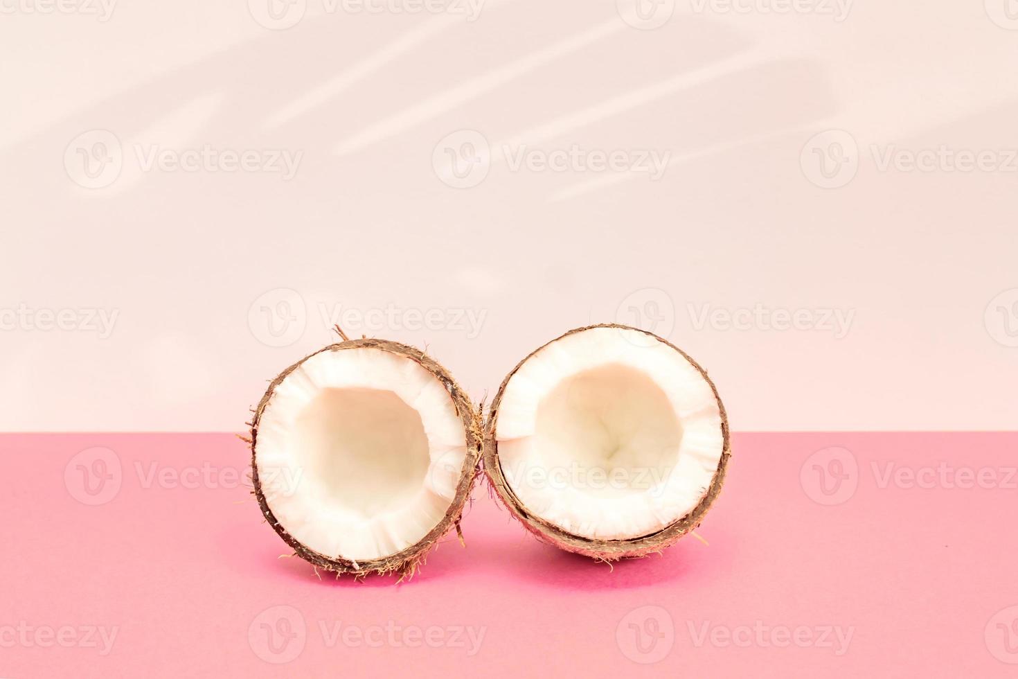 två halvor av färsk rå kokos på rosa backgound med kight skuggor i vit. foto