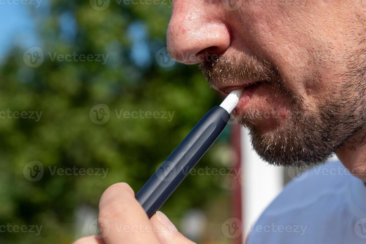 skäggig man rökning e-cigarett utomhus. uppvärmning tobak systemet, tobak produkt teknik. foto