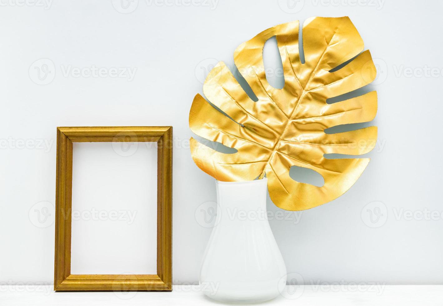 guld och vit interiör attrapp design. tömma fotoram och monstera blad jag är vit vas på vit vägg bakgrund. trendig design foto