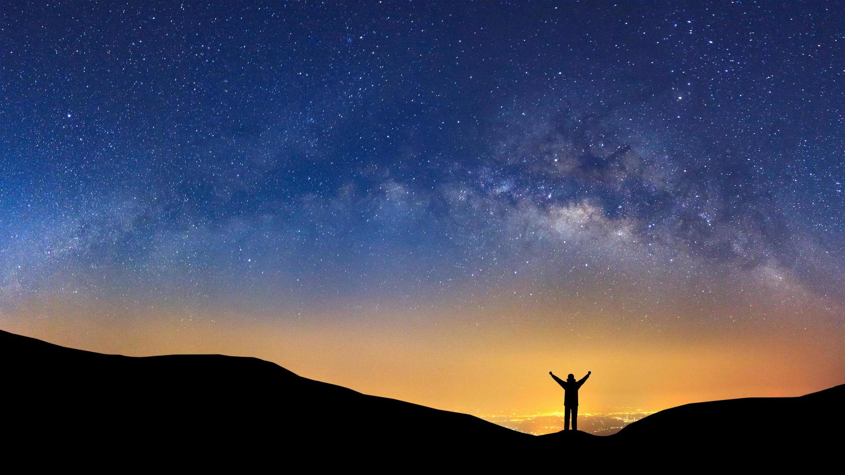 panorama landskap med mjölkig sätt, natt himmel med stjärnor och silhuett av en stående sportig man med Uppfostrad upp vapen på hög berg. foto