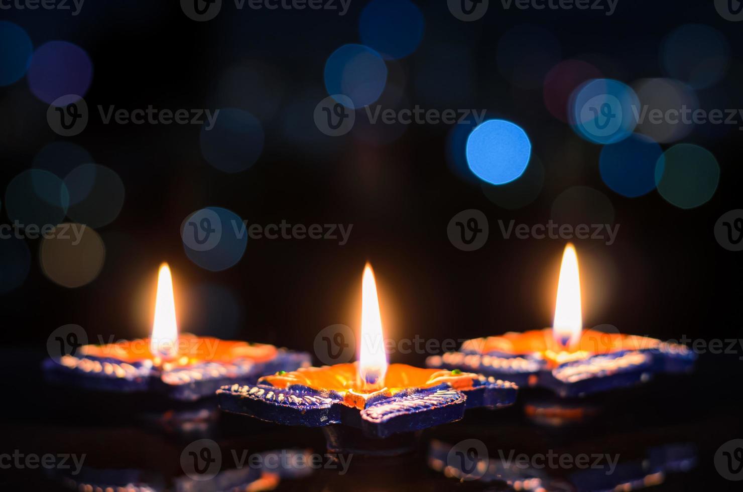 selektiv fokus på flamma av först lera diya lampor belyst på mörk bakgrund med färgrik bokeh lampor. diwali festival begrepp. foto