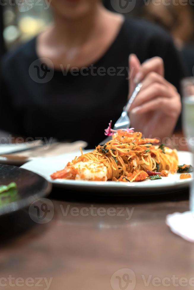 stänga upp och fokus på de spaghetti nudel i de vit maträtt vit fläck svart klänning kvinna hand och henne gaffel på Det. foto