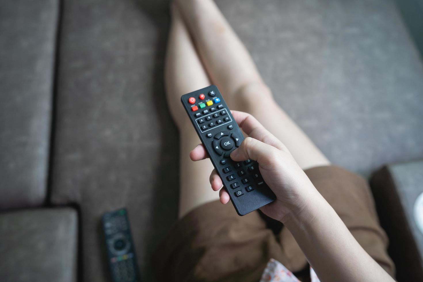 stänga upp tv avlägsen kontrollera i ung kvinna rosa skjorta händer pekande till TV uppsättning och vändning den på eller av. Välj kanal tittar på TV på soffa på Hem i de levande rum koppla av. foto