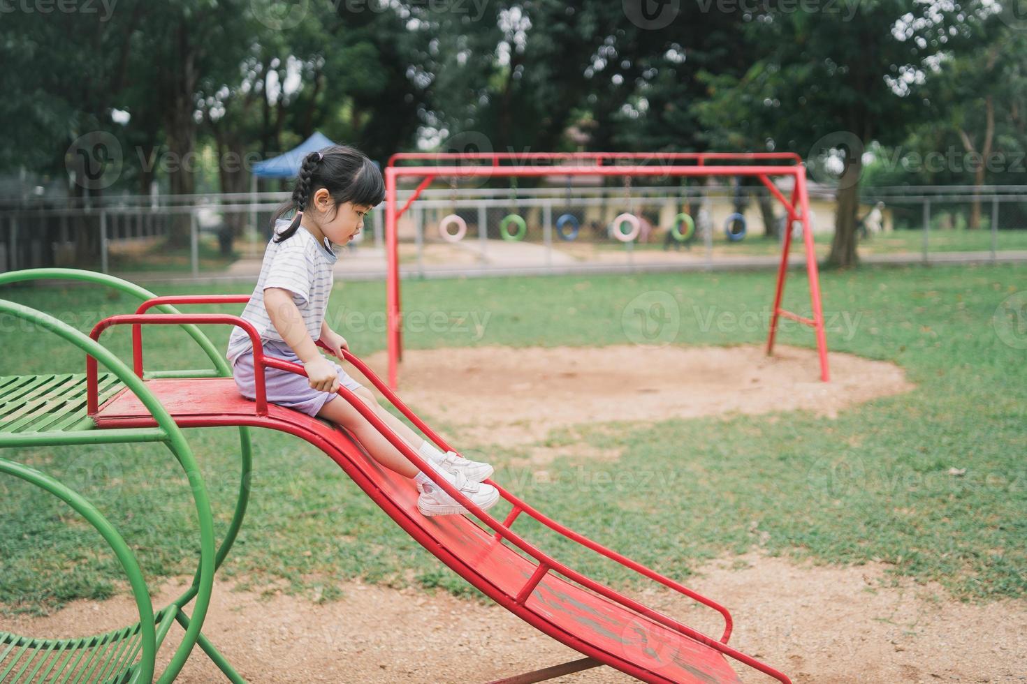 söt asiatisk flicka leker på skolan eller dagis gården eller lekplatsen. hälsosam sommaraktivitet för barn. liten asiatisk flicka som klättrar utomhus på lekplatsen. barn som leker på utomhuslekplatsen. foto