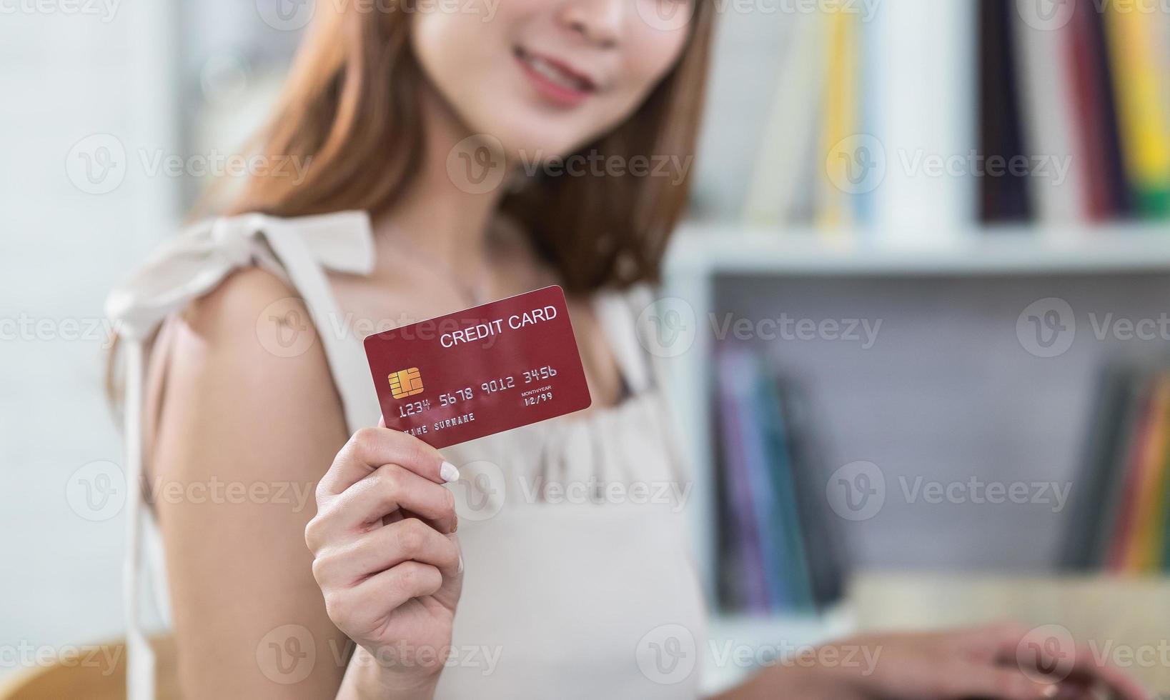 kvinna innehav som visar kreditera kort till handla uppkopplad. asiatisk kvinna arbetssätt på Hem. uppkopplad handla, e-handel, internet bank, utgifterna pengar, arbetssätt från Hem begrepp. foto