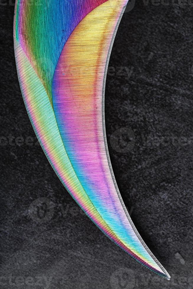 de böjd skarp blad av de kerambit dolk är en lutning regnbåge Färg på en mörk bakgrund. foto