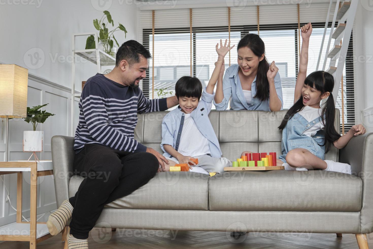 lycklig asiatisk härlig thailändsk familjeomsorg, pappa, mamma och små barn har roligt när de leker med färgglada leksaksblock tillsammans på soffan i det vita vardagsrummet, fritidshelgen och livsstilen för välbefinnande i hemmet. foto