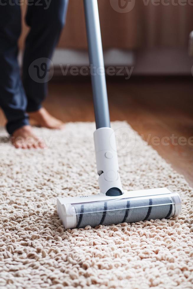 mänsklig ben och en vit turbo borsta av en sladdlös Vakuum rengöringsmedel rengör de matta i de hus foto
