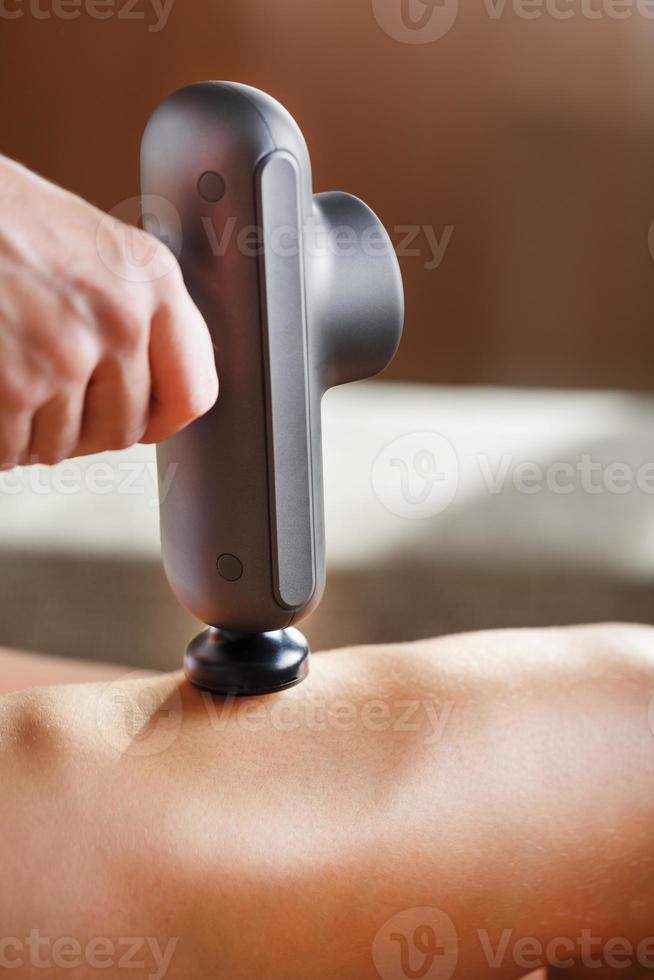 massage av kvinnors ben med en chock massage enhet. foto