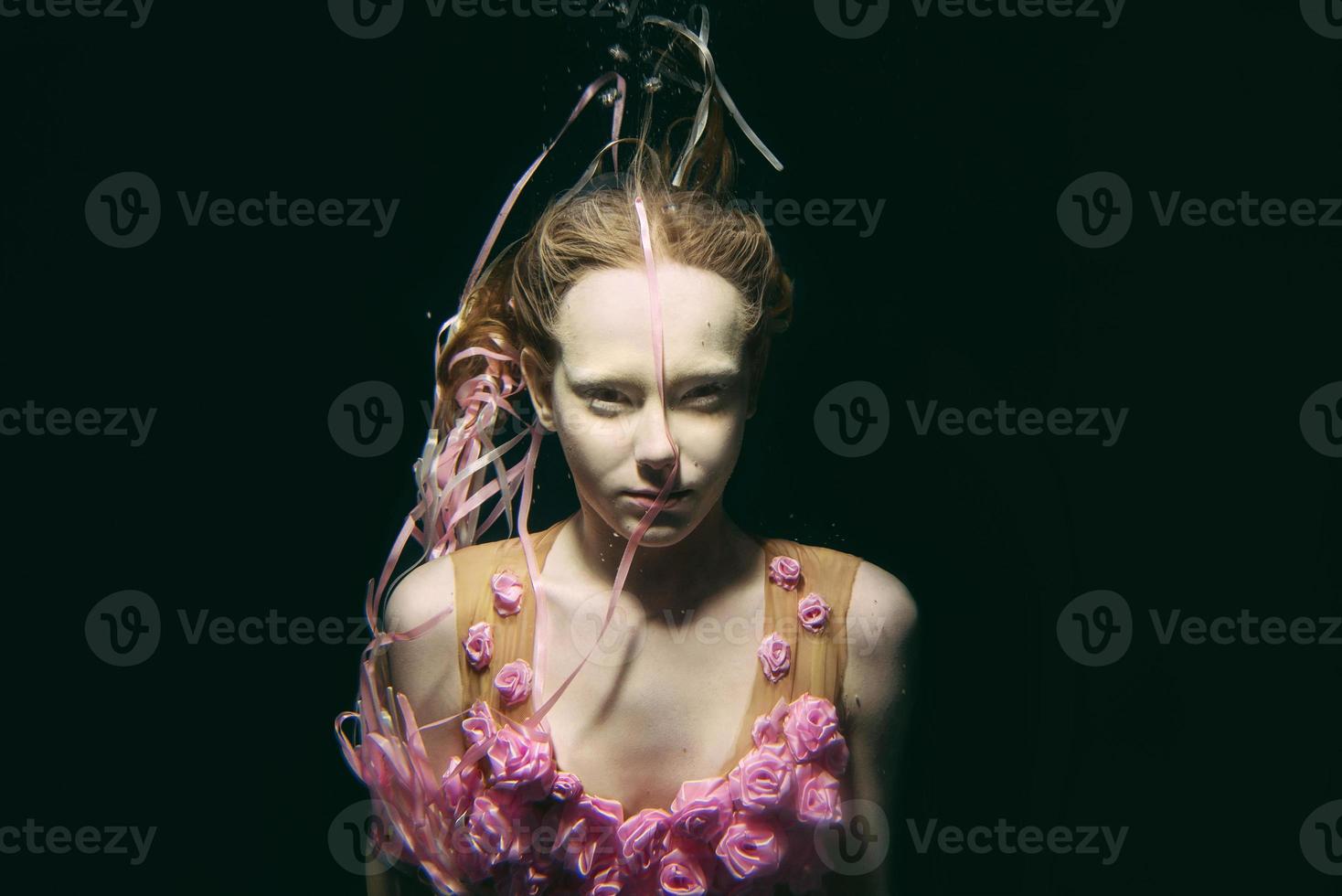 ung rödhårig flicka i klänning tillverkad av ro under vattnet foto