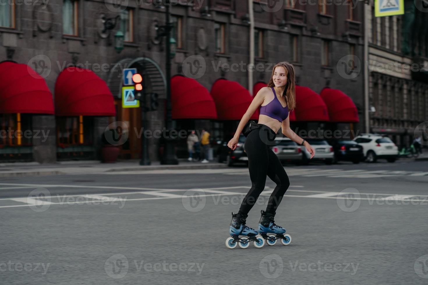 nöjd sportig kvinna åker på rullar i urban plats leder hälsosam livsstil klädd i sportkläder tittar bort har glada uttryck tycker om konditionsträning. sport aktivitet hobby rekreation foto